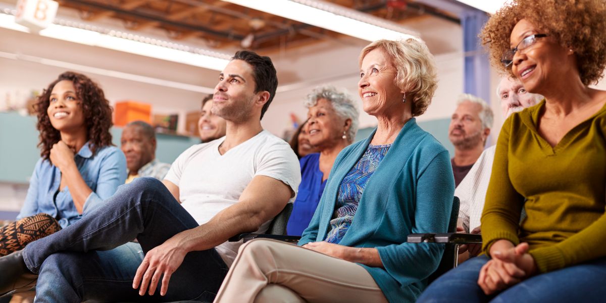 Diverse group of people sitting and smiling at a community event indoors.