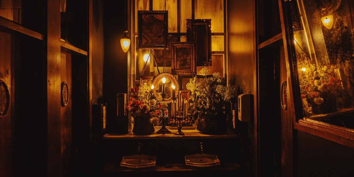 A moody, antique-style bathroom with vintage lighting, ornate mirrors, and floral arrangements — highlighting why it may be time to remodel your bathroom in a classic New Orleans home.